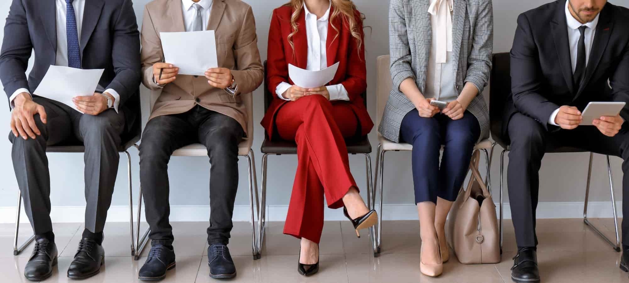 Interview candidates sitting in a row. They are studying their phones or pieces of paper.